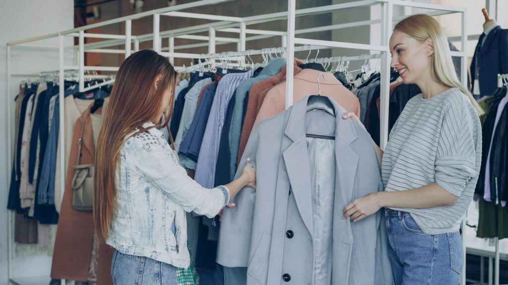 Shop assistant helping a customer choose a coat from the rails in a clothing boutique