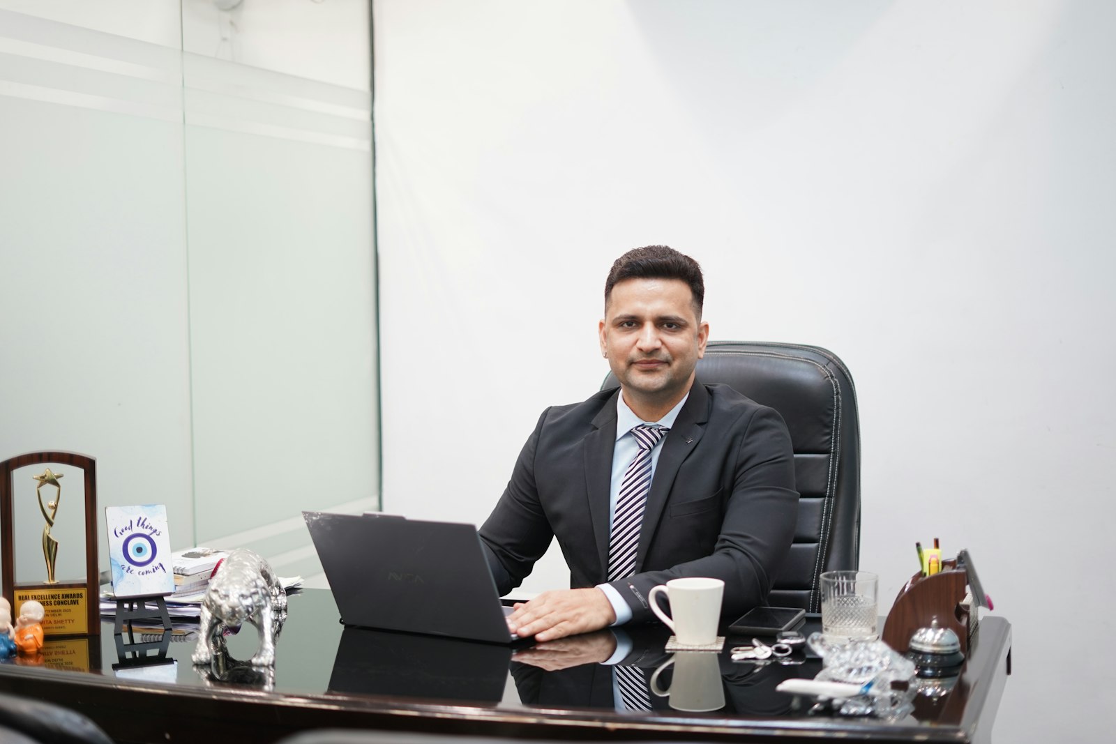 Man in a suit sitting at a desk with a laptop and coffee